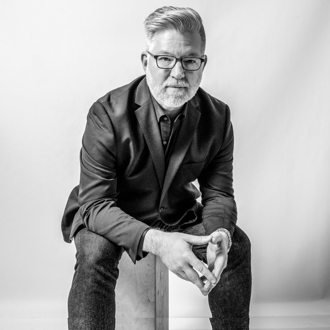 Portrait of baritone Jason Awbrey, seated in a black jacket, in black and white.